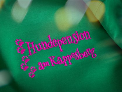 Gr&uuml;nes Shirt mit pinkfarbener Logostickerei und Pfotenspur f&uuml;r die Hundepension am Kappesberg in Breitscheid-Medenbach